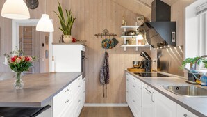 Una cocina moderna con paredes de madera, armarios blancos, una isla central, luces colgantes y un reloj en la pared.