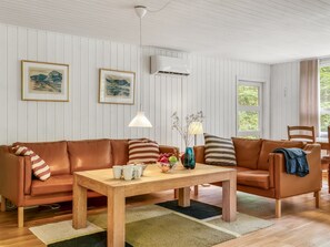 Un salon chaleureux avec un canapé en cuir marron, une table basse en bois et deux œuvres d’art encadrées accrochées au mur.