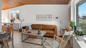 Ett modernt vardagsrum med ett träpanelat tak, en brun lädersoffa, ett soffbord och utsikt genom stora fönster.
