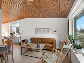 Ein modernes Wohnzimmer mit Holzboden, einem braunen Ledersofa, einem Couchtisch und Blick durch große Fenster.