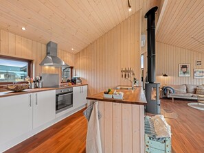 A modern kitchen with wooden walls, a large stove, and a dining area with a sofa. - "Tamara" - 800m to the fjord by Interhome (Tarm)