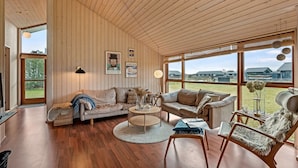 Un salón amplio con paredes de madera, un ventanal grande, un sofá, una mesa de centro y una silla.