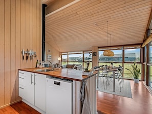 A modern kitchen with wooden cabinets, a dishwasher, and a dining area with a table and chairs. - "Tamara" - 800m to the fjord by Interhome (Tarm)