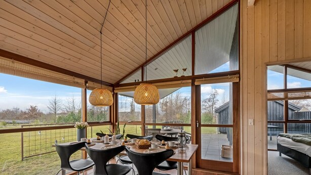 Un patio techado con una mesa lista para comer, ventanas amplias y vistas al exterior.