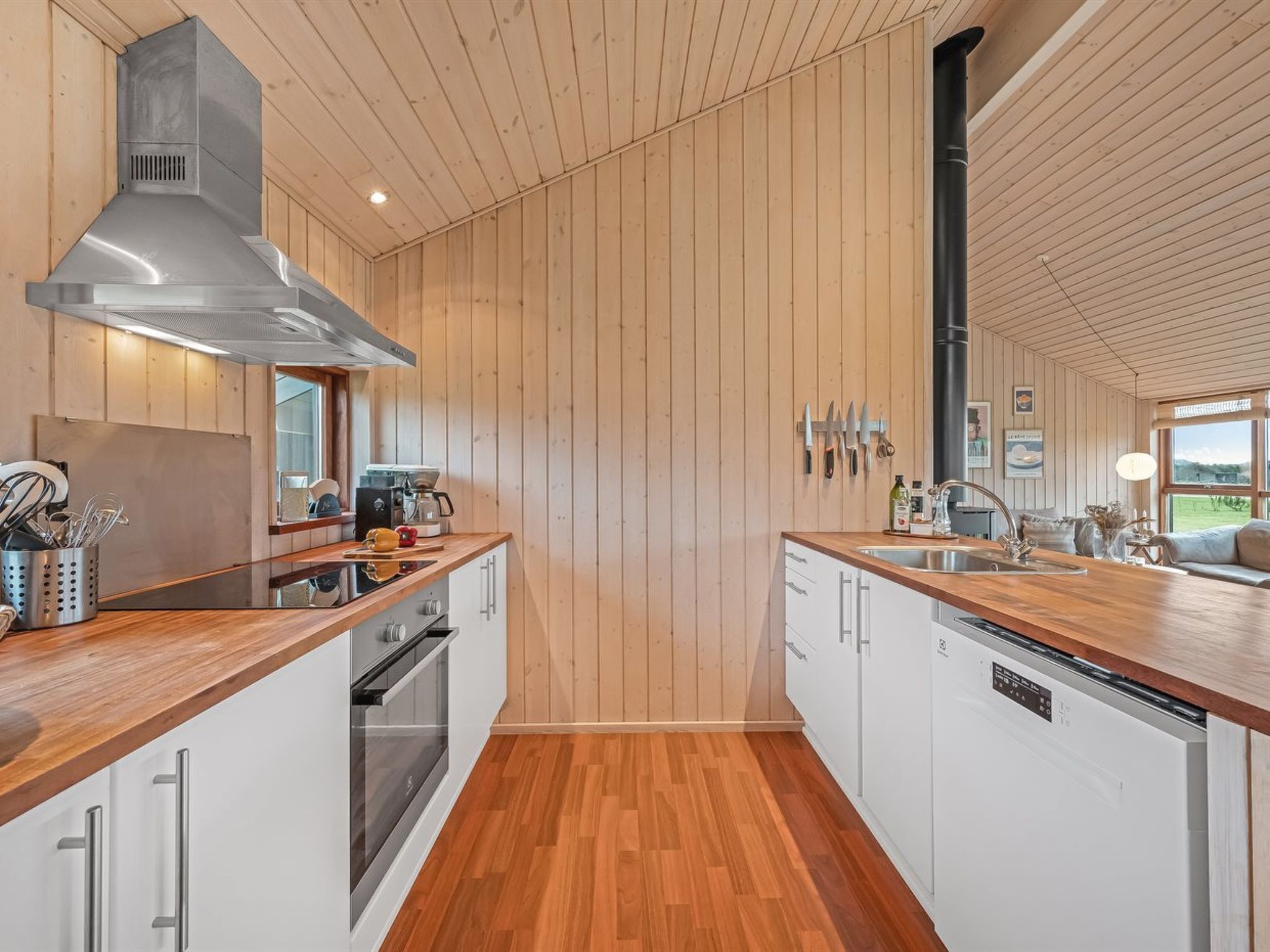 A modern kitchen with wooden paneling, a stainless steel range hood, and a dishwasher.