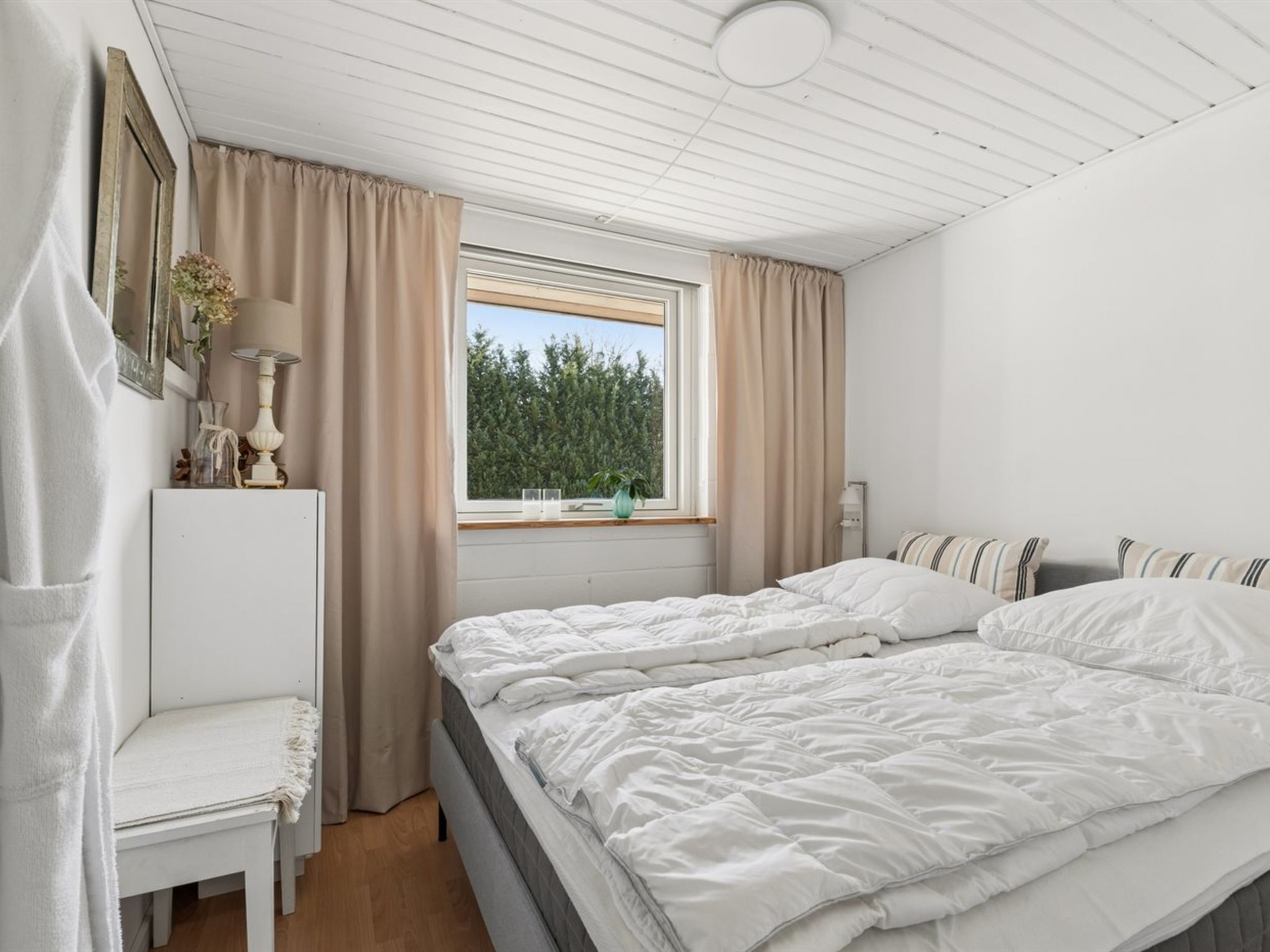 A bedroom with two beds, a window with curtains, a bedside table, and a lamp.
