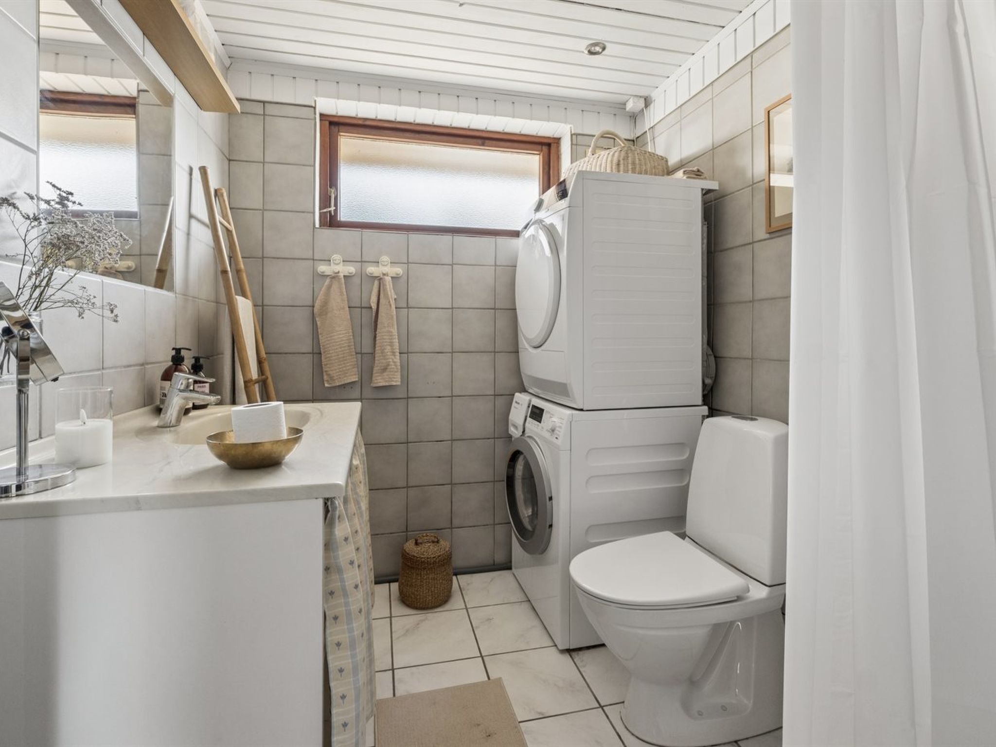 A compact bathroom with a washing machine, toilet, and a small window.