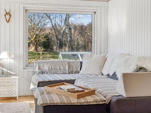 Ein Schlafzimmer mit großem Fenster, einem Bett mit Holztischchen, einem weißen Nachttisch und einem an der Wand befestigten Tierkopf.
