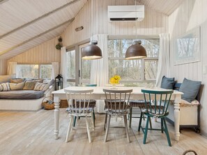 Ein gemütliches Zimmer mit Holzbalkendecke, einem Esstisch mit Stühlen, einer Couch und einem Fenster mit Vorhängen.