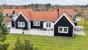 Een rij zwarte houten huizen met rode daken en witte details, omringd door groen gras en bomen.