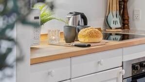 Een keuken met een koffiezetapparaat, een broodje, een glas en een plant.