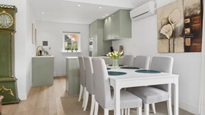 Een eetgedeelte met een witte tafel, grijze stoelen en een bloevas.