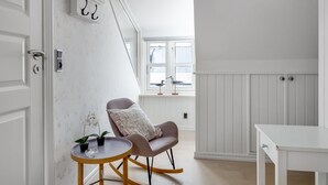 Et værelse med en hvid dør, et lille rundt bord med en stol, et vindue med udsigt og en hvid væg med en dørklokke.