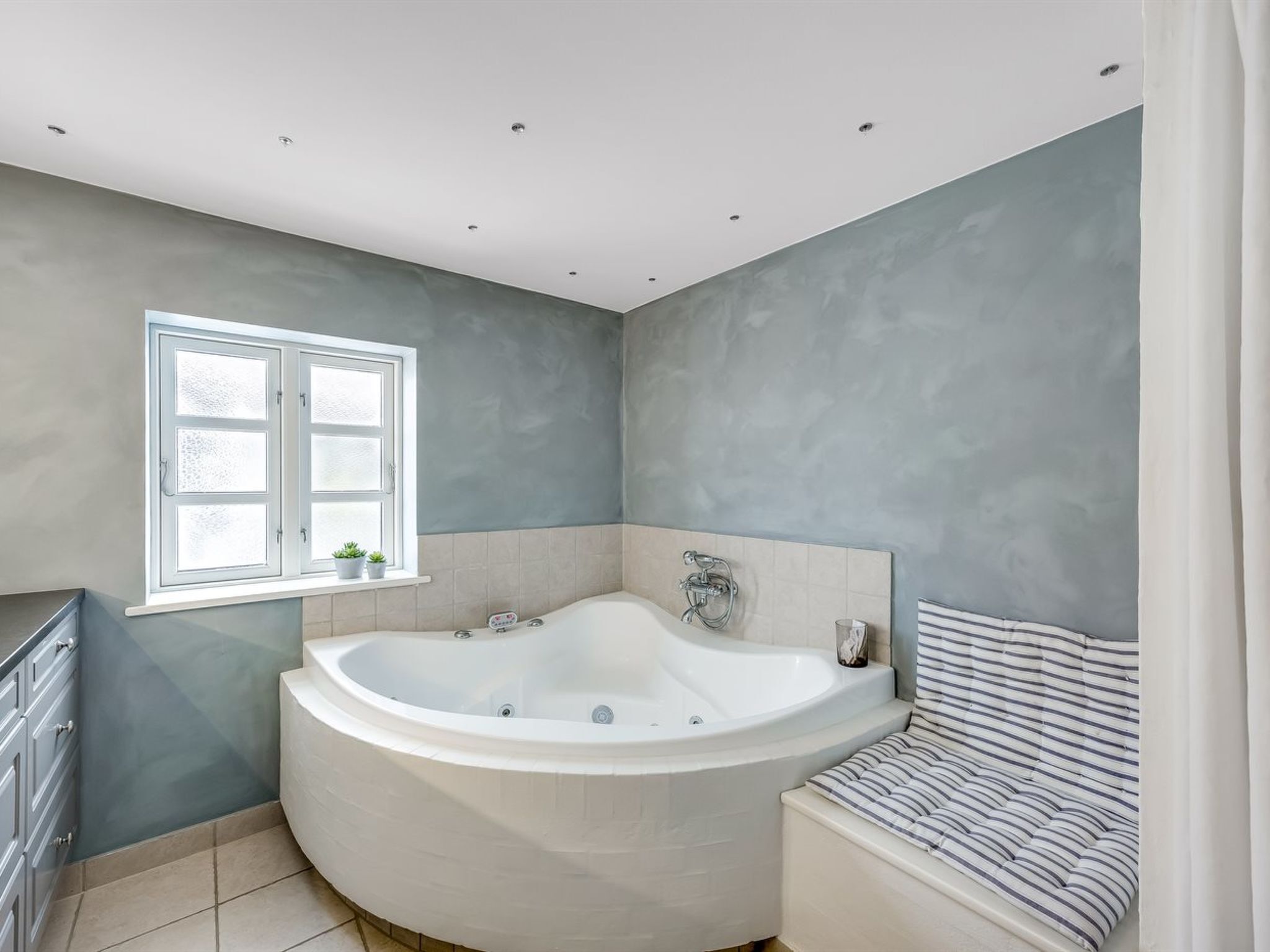 Ein modernes Badezimmer mit einer freistehenden Badewanne, einem Fenster und einer gestreiften Sitzbank.