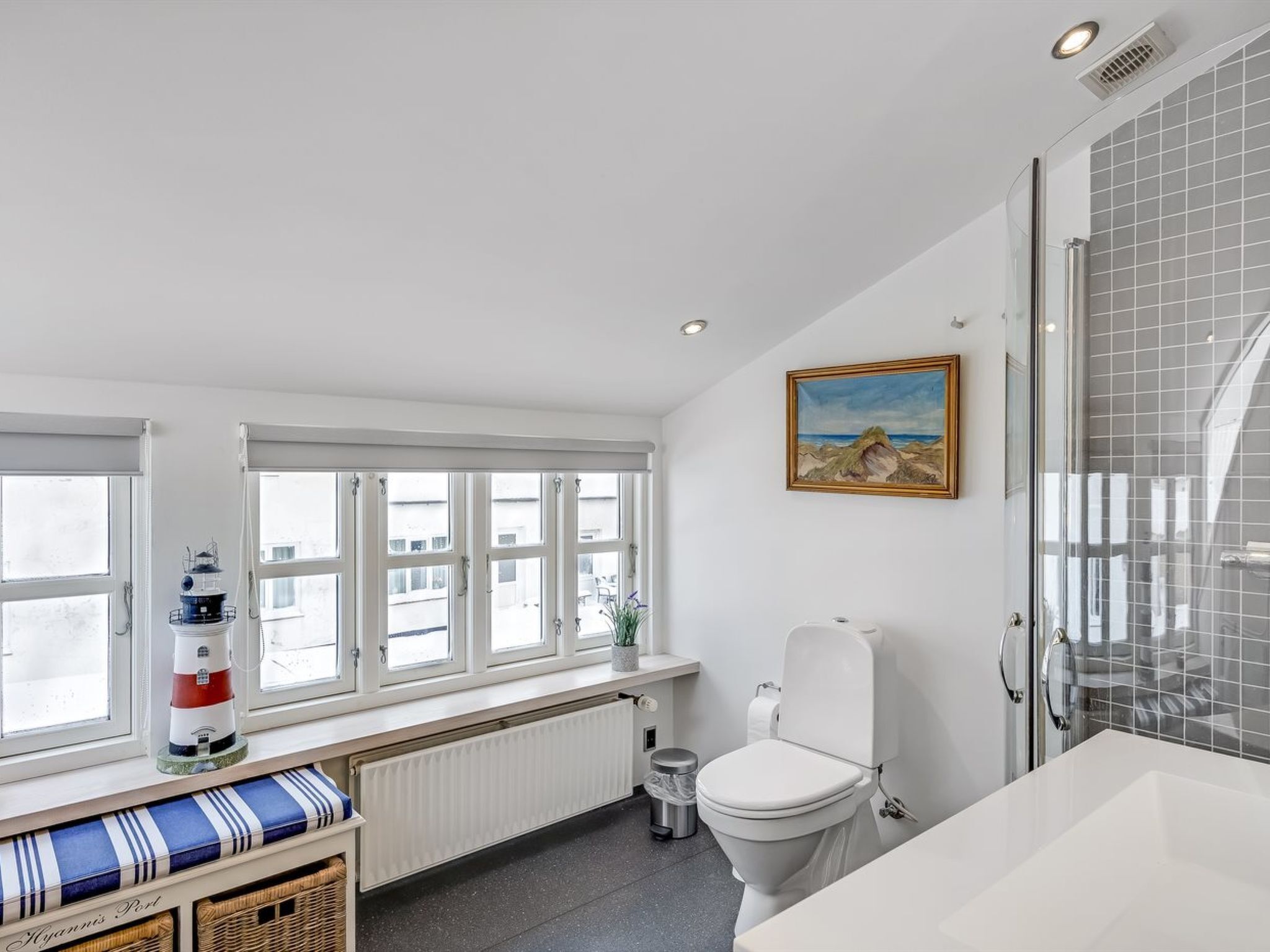 Un baño con inodoro, lavabo, ventana con vistas y un cuadro en la pared.