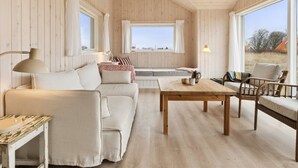 Ein gemütlicher Raum mit Holzvertäfelung, einer Couch, einem Couchtisch und einem Korbstuhl.