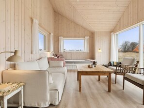 Ein gemütlicher Raum mit Holzvertäfelung, einer Couch, einem Couchtisch und einem Korbstuhl.