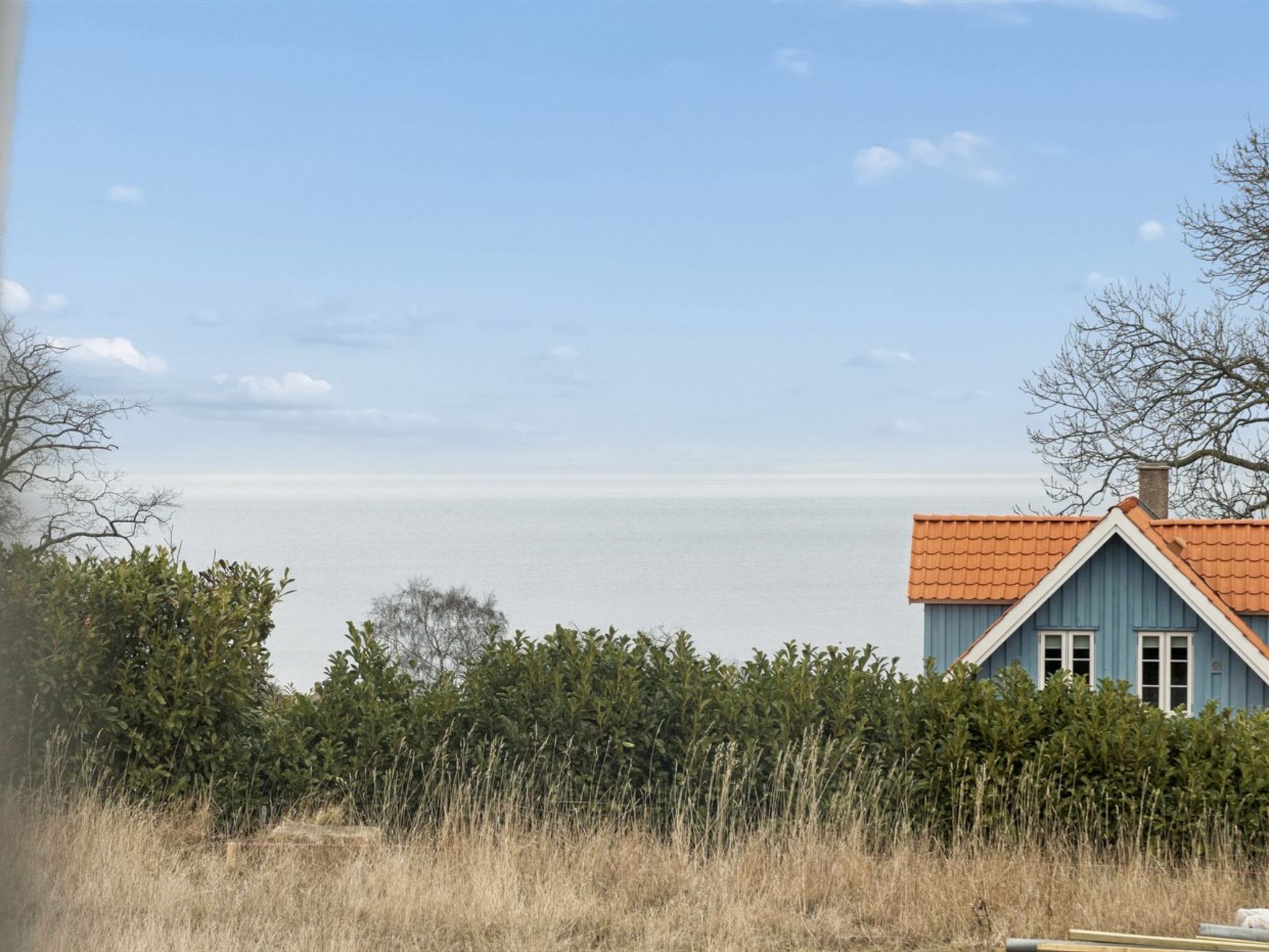 A house with a red roof, surrounded by dense foliage and a clear view of the sea.