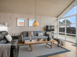Ein modernes Wohnzimmer mit einer Couch, einem Couchtisch, einem Fernseher und großen Fenstern.