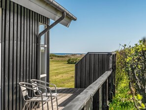 Ein Holzgebäude mit einem Balkon, Metallstühlen und Blick auf den Strand.