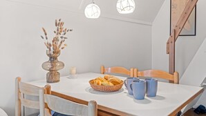 Un comedor con una mesa, sillas, un jarrón con plantas secas, una cesta de pan y dos lámparas colgantes.