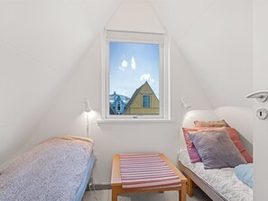 Ein kleines, dreieckiges Schlafzimmer im Dachgeschoss mit Fensterblick auf ein Haus, einem Nachttisch und einem Bett mit Kissen.