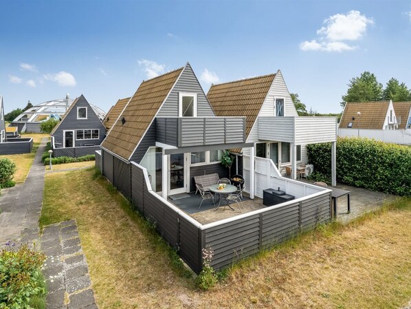 Une maison moderne dotée d’un patio couvert, d’un petit jardin et d’une maison voisine.