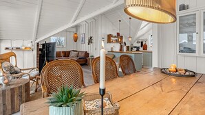 Een ruime loft met hoge plafonds, een eethoek met een houten tafel en rieten stoelen, een keuken met een centraal kookeiland en een gezellige zithoek met een bank en fauteuils.