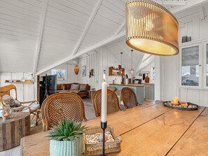 Ein geräumiger Loft mit hohen Decken, einem Essbereich mit Holztisch und Korbstühlen, einer Küche mit Kochinsel und einer gemütlichen Sitzecke mit Sofa und Sesseln.
