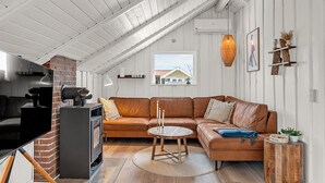 Een loft-achtige woonruimte met een houten plafond, een open haard van baksteen, een leren bank, een ronde houten tafel en een klein bijzettafeltje.