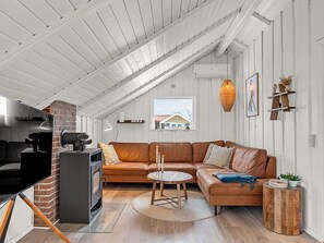 Ein Loft-Wohnraum mit Holzboden, einem Kamin aus Ziegeln, einem Ledersofa, einem runden Holztisch und einem kleinen Beistelltisch.