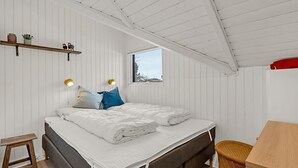 Een slaapkamer met een bed, bedlampen, een raam, een tafeltje en een plank met decoratieve objecten.