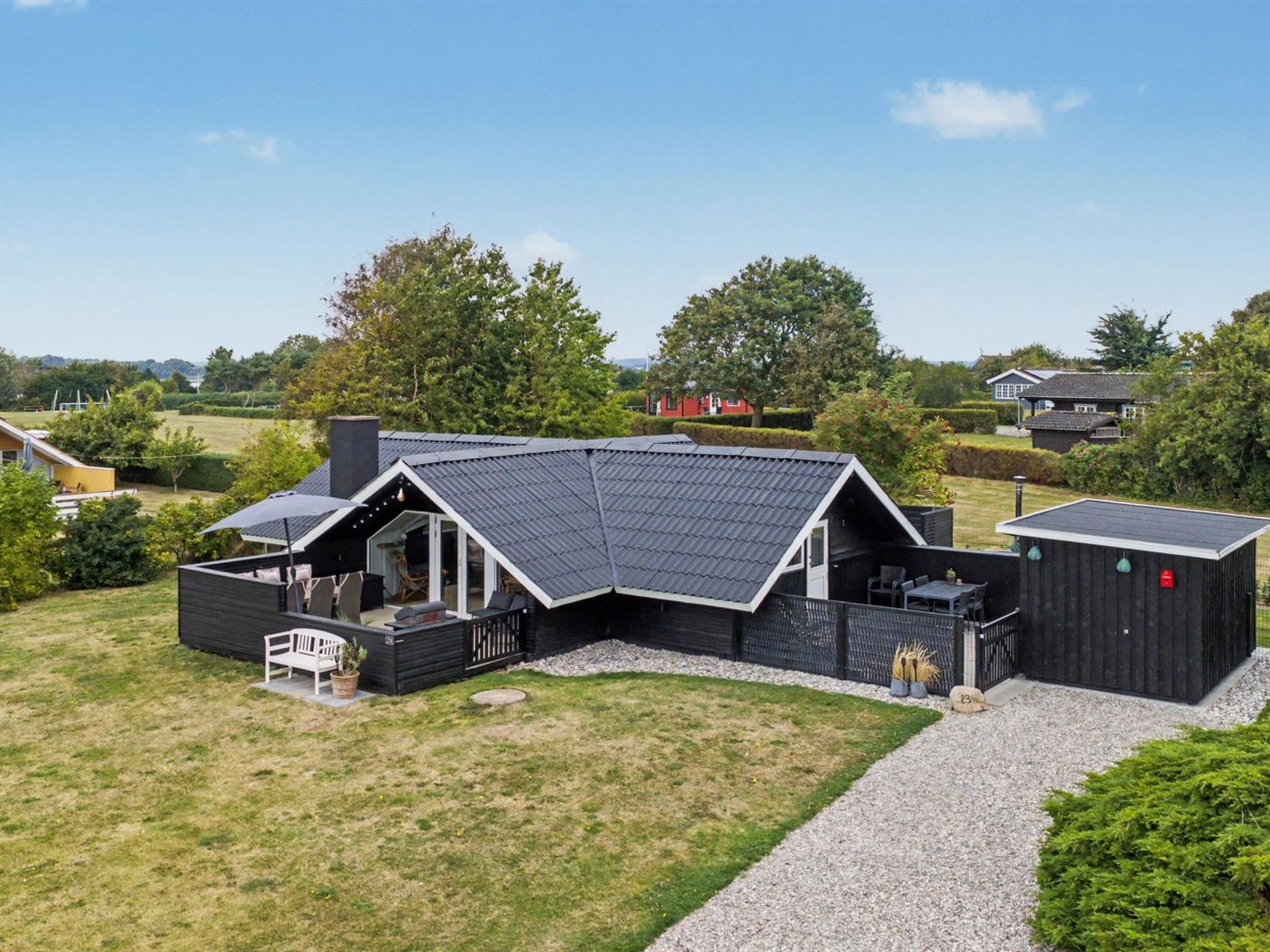 Ein modernes Haus mit geneigtem Dach, einer überdachten Terrasse und einem Schotterweg.