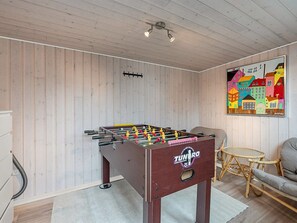 Ein Zimmer mit einem Kicker, einem Korbstuhl, einer Couch und einem farbenfrohen Bild an der Wand.