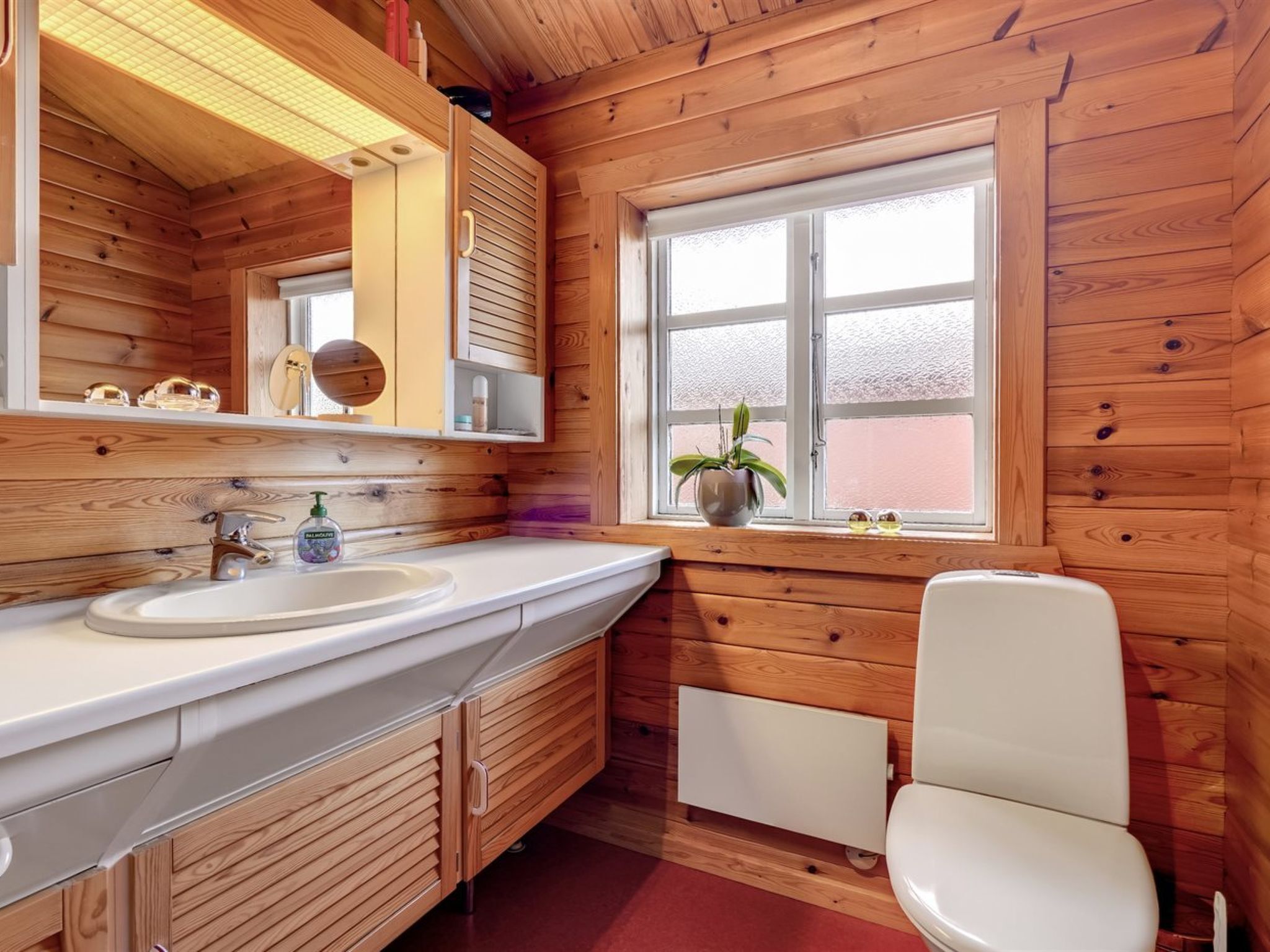 A wooden cabin bathroom with a sink, mirror, and toilet.