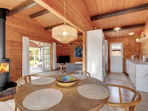 Interno di una baita in legno con tavolo da pranzo, sedie, camino, televisione e angolo cottura.