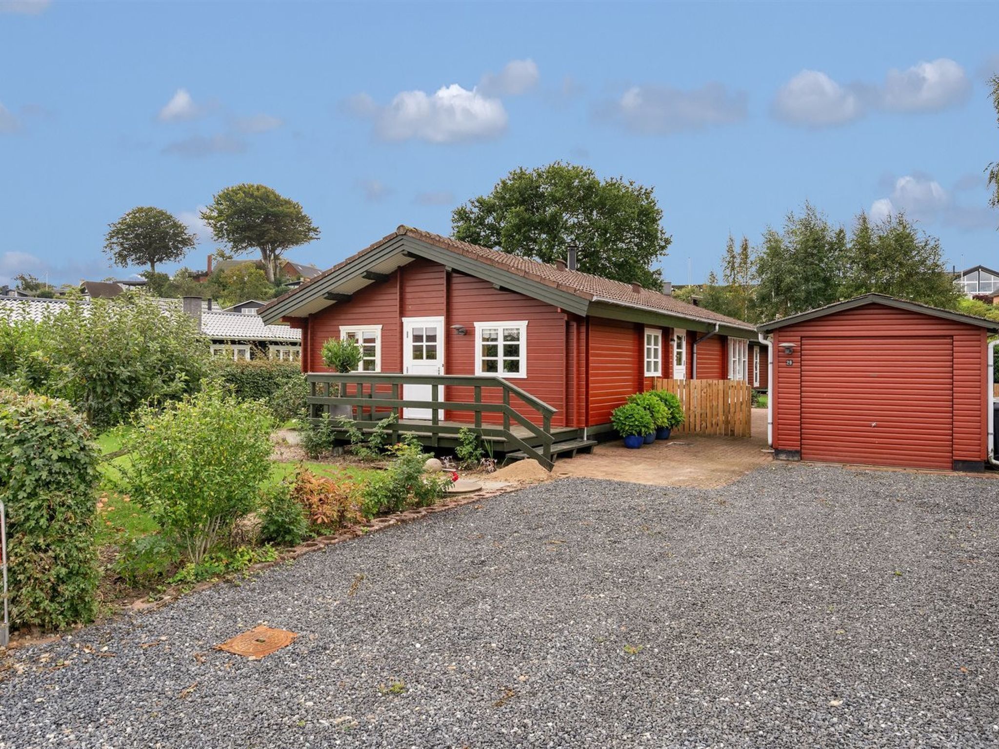 A red building with a gravel driveway, a wooden bridge, and a fenced garden area.