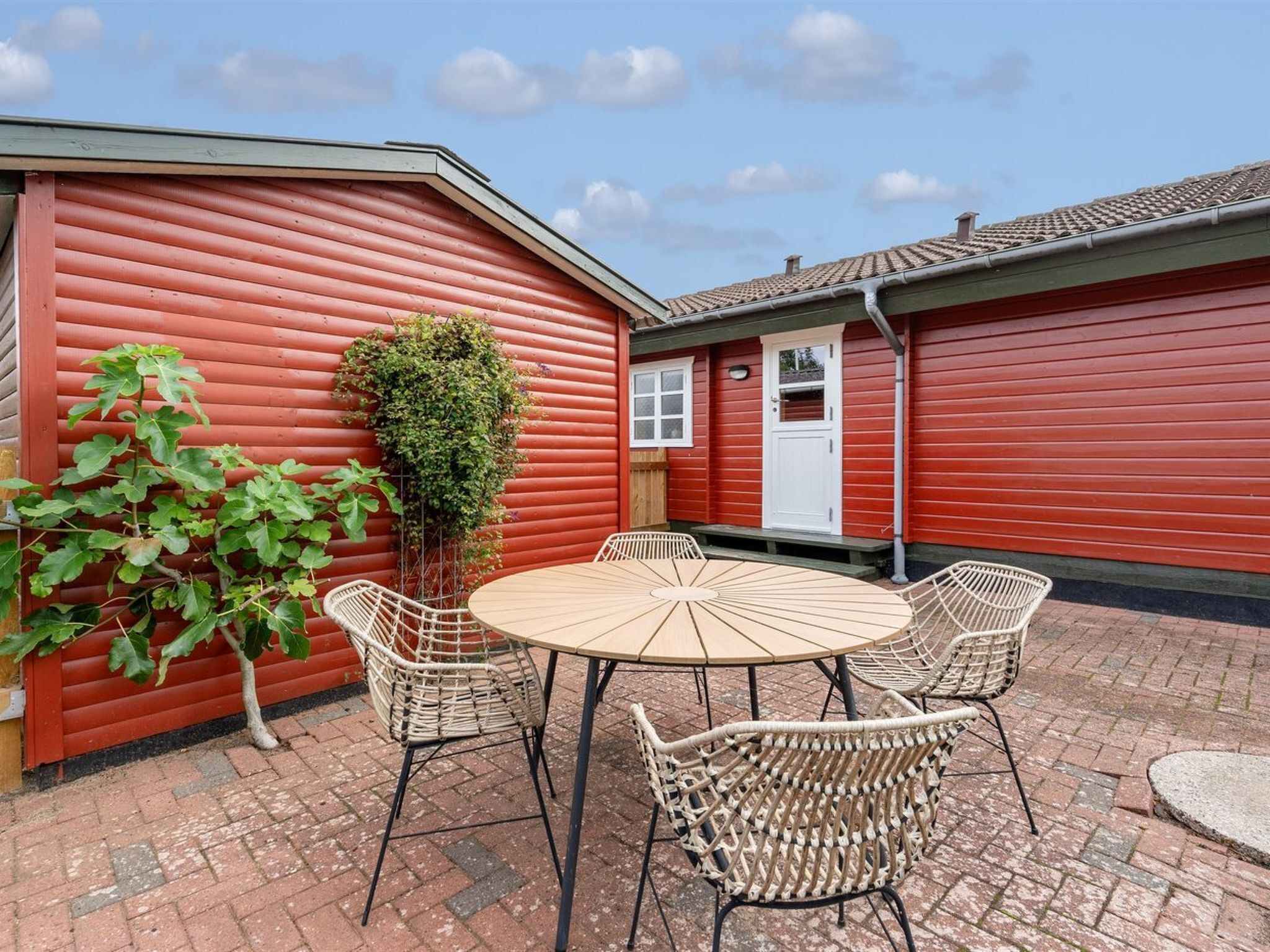 A red building with a white door, a round table with chairs, and a potted plant.