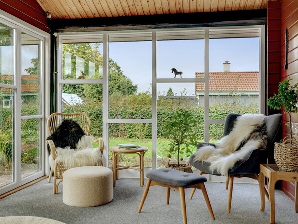 A cozy room with a large window, a wooden ceiling, and a view of the garden.