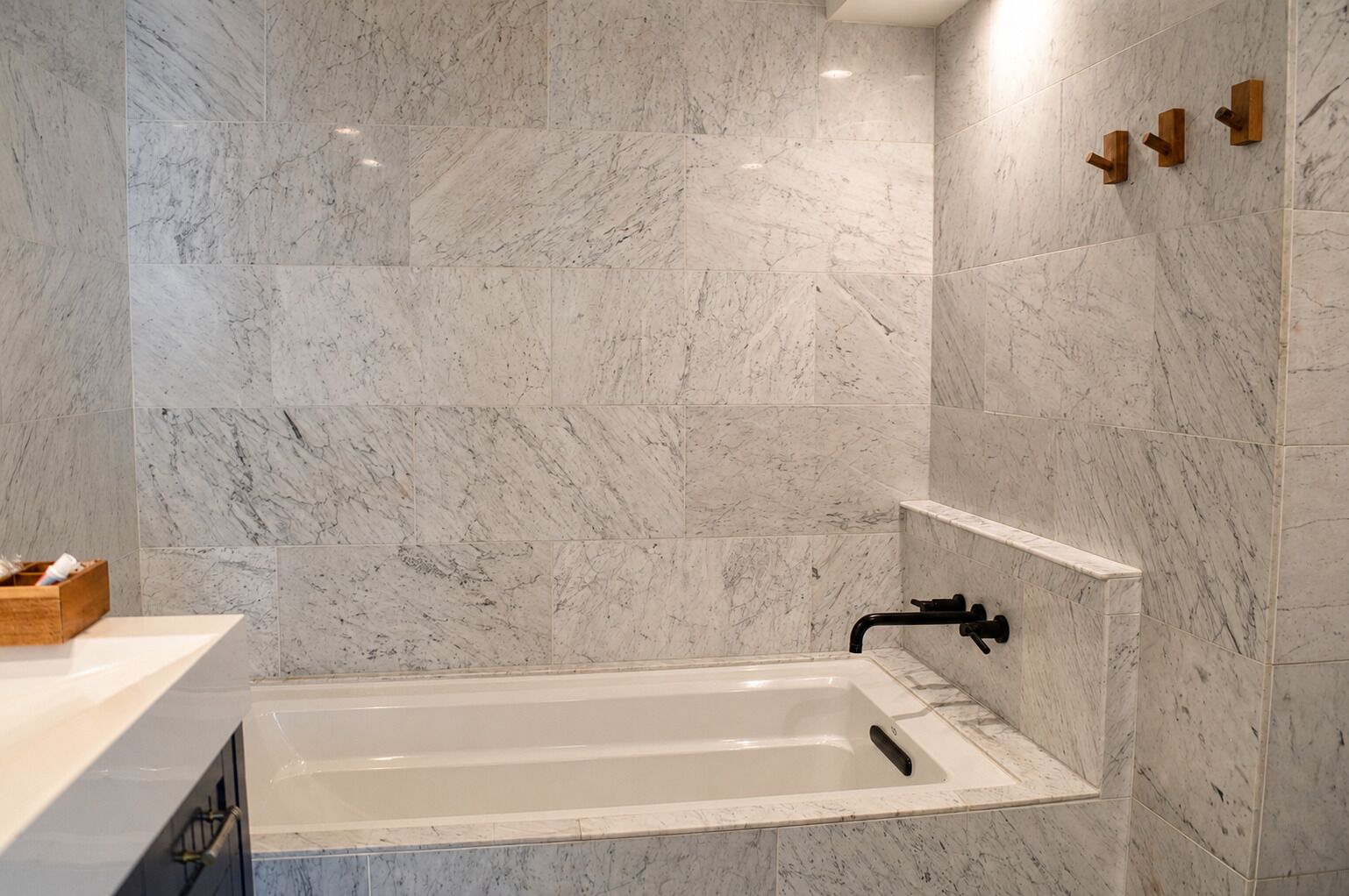 A bathroom with a bathtub, marble walls, and a wooden shelf.