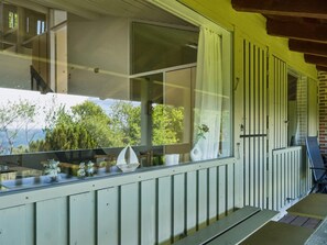 Ein Balkon mit Geländer, ein Fenster mit Vorhang und Blick auf Bäume und Berge.