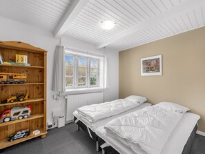 Ein Schlafzimmer mit zwei Betten, einem Holzregal für Spielzeug, einem Fenster, einer Heizung und einem gerahmten Bild an der Wand.