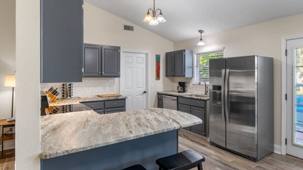 A modern kitchen with grey cabinets, a stainless steel refrigerator, a marble countertop, and a pendant light. - Candlewood Casa ~ 3BR/2BA 15 Mins to Beach! (Navarre)