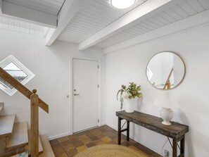 Eine Treppe mit Holzbodenstufen, eine weiße Tür, ein runder Spiegel, ein kleiner Tisch mit Blumen in einer Vase und ein Ausblick durch ein Oberlicht.