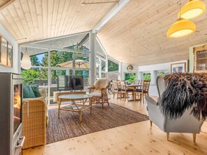 A modern living room with a fireplace, large windows, and a dining area.