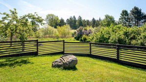 Ein eingezäunter Außenbereich mit einem großen Felsen in der Mitte, umgeben von üppiger Bepflanzung und Bäumen.