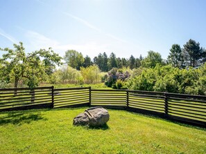 A fenced outdoor area with a large rock in the center, surrounded by lush greenery and trees.