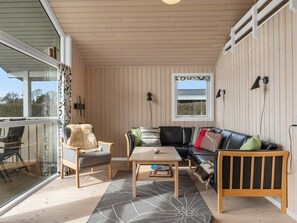 Ein gemütliches Zimmer mit Holzbalkendecke, einem großen Fenster, einer Couch, einem Sessel und einem Tisch.