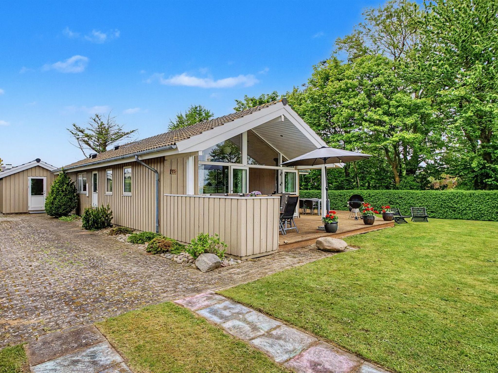 Een gelijkvloers huis met een overdekte patio, een kleine tuin en een geplaveid oprit.