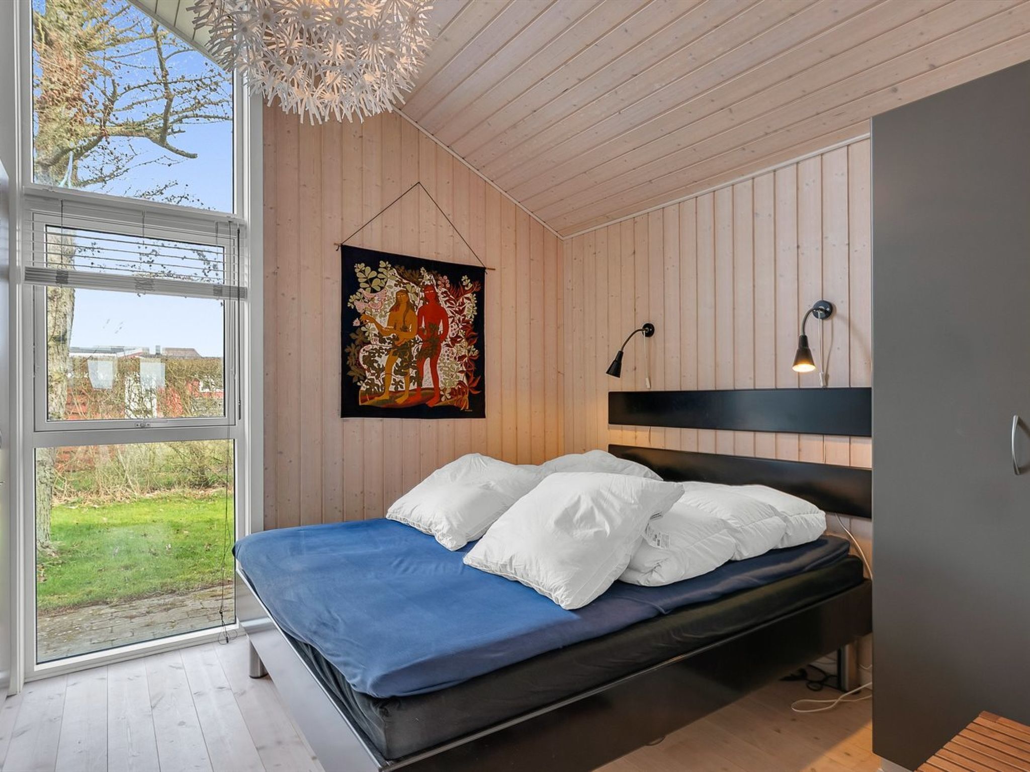 Ein Schlafzimmer mit Bett, einem Wandbild, einem Fenster und einer Deckenleuchte.